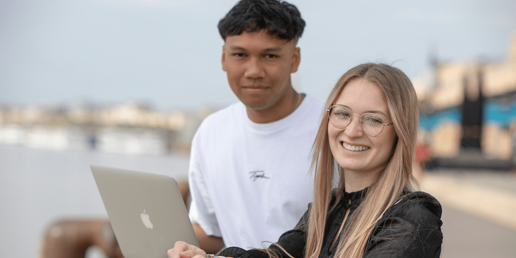 deux étudiants de l'école de commerce INSEEC installés en extérieur autour d'un ordinateur et souriant