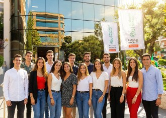 Groupe d’étudiants devant l’entrée vitrée d’un campus à Barcelone, avec deux drapeaux EU Business School et une façade reflétante en arrière-plan