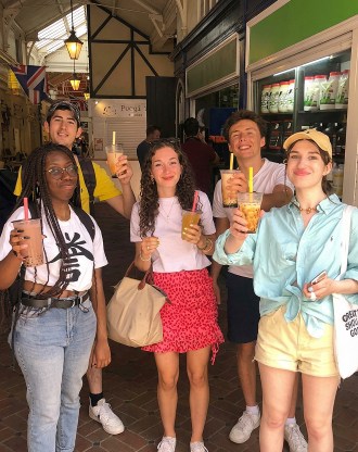 Groupe d’étudiants souriants tenant des boissons dans un marché couvert, posant ensemble lors d’une sortie conviviale
