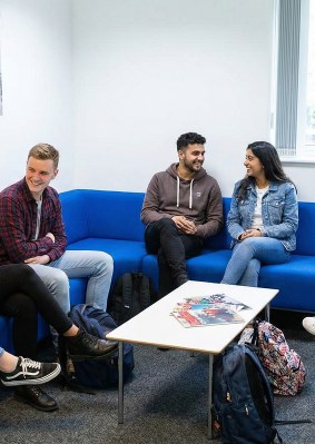 Groupe d’étudiants discutant dans un espace de détente du campus OMNES Education à Londres, assis sur des canapés bleus autour d’une table basse