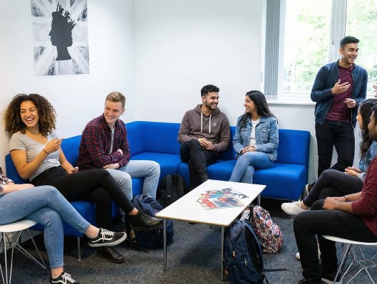 Groupe d’étudiants discutant dans un espace de détente du campus OMNES Education à Londres, assis sur des canapés bleus autour d’une table basse