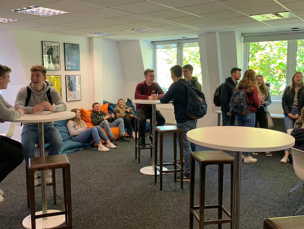 Étudiants INSEEC discutant et se relaxant dans un espace de détente lumineux avec tables hautes et poufs colorés