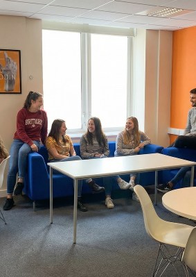 Groupe d’étudiants réunis dans un espace commun du campus OMNES Education à Londres, assis sur des canapés bleus et échangeant de façon décontractée