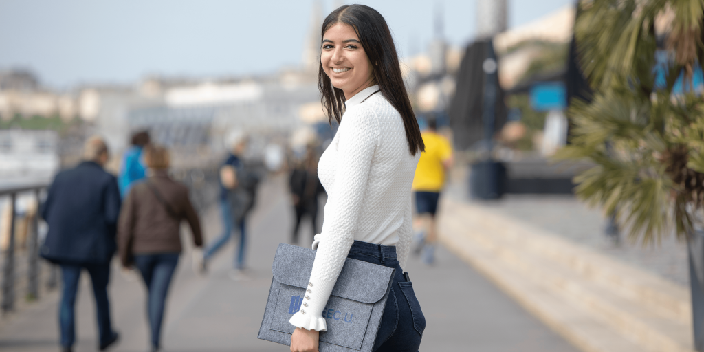 INSEEC business school student outside holding a computer case and smiling